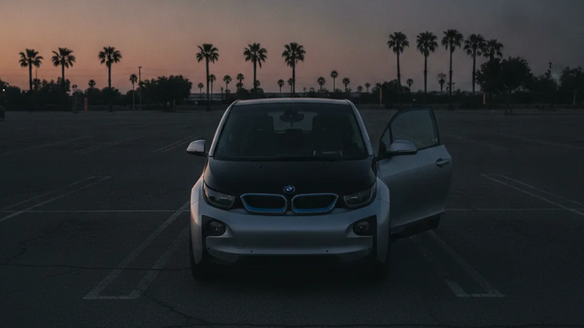 A BMW i3 city EV parked in a dim San Diego setting with a dark, unlit dashboard, illustrating a dead 12V battery.